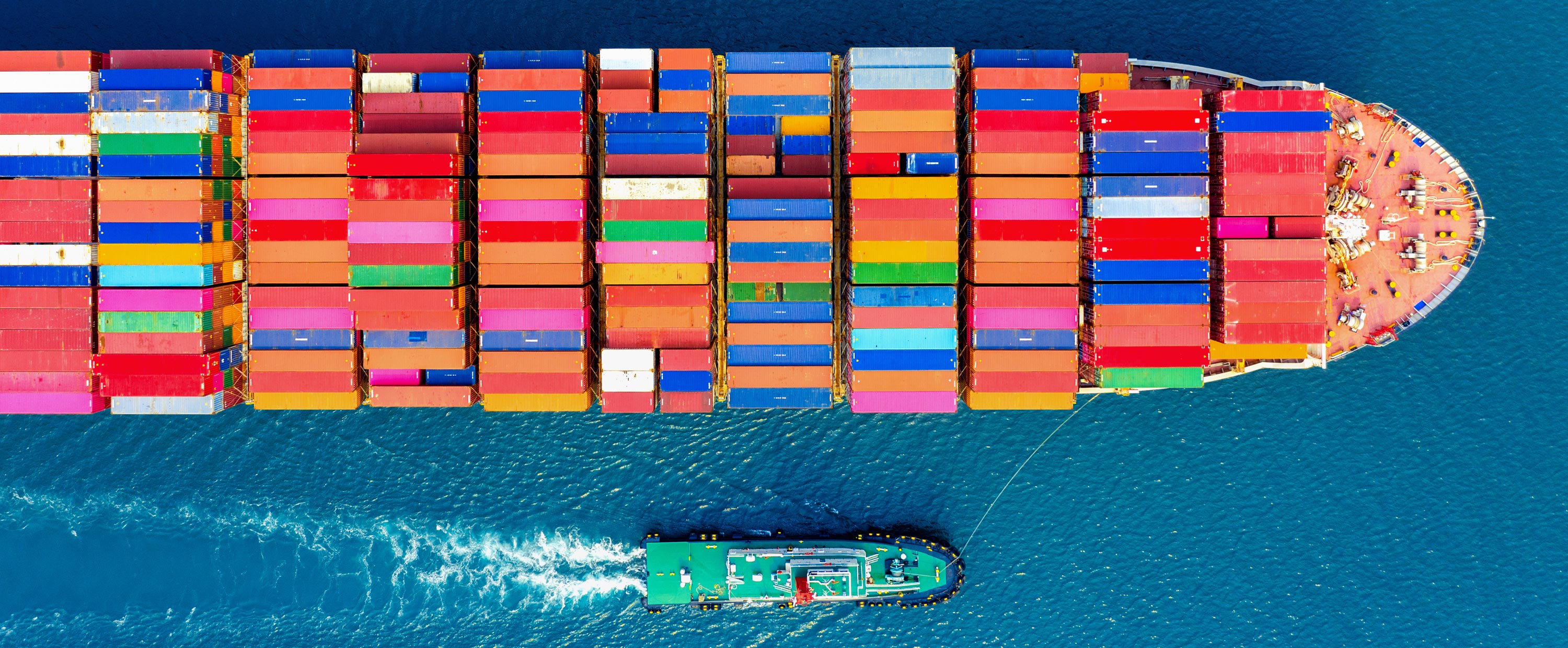 Riesiges Containerschiff im azurblauen Ozean befüllt mit Handelswaren aus aller Welt für B2B. Bunte Container transportieren Waren wie Medizinische Produkte und Geräte, Rohkaffe, Rohkakao, weitere Agrarprodukte. Am Handelsschiff ist ein kleineres Schiff.